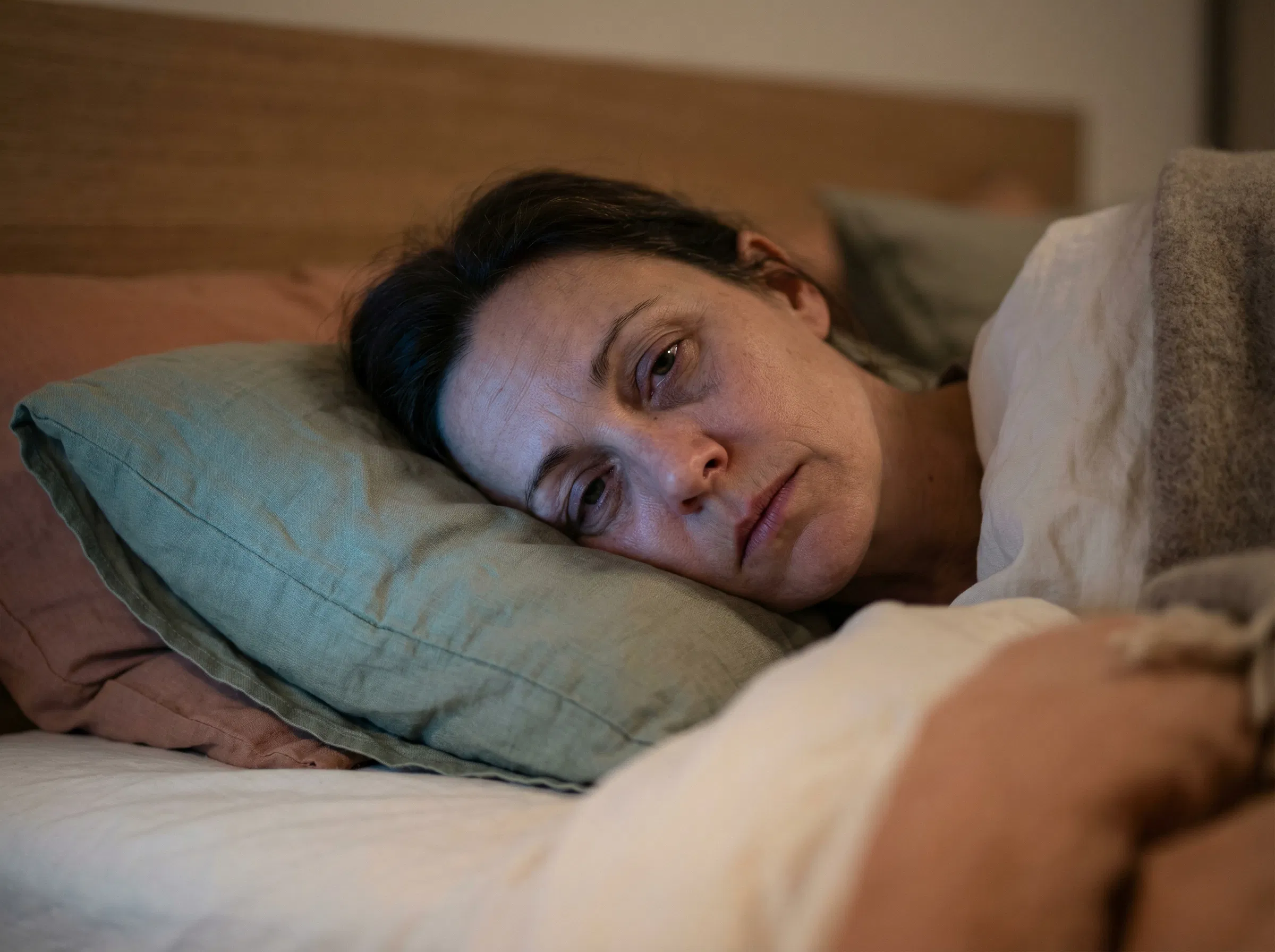 Rostro exhausto de mujer en la almohada con ojeras, incapaz de dormir a pesar del cansancio