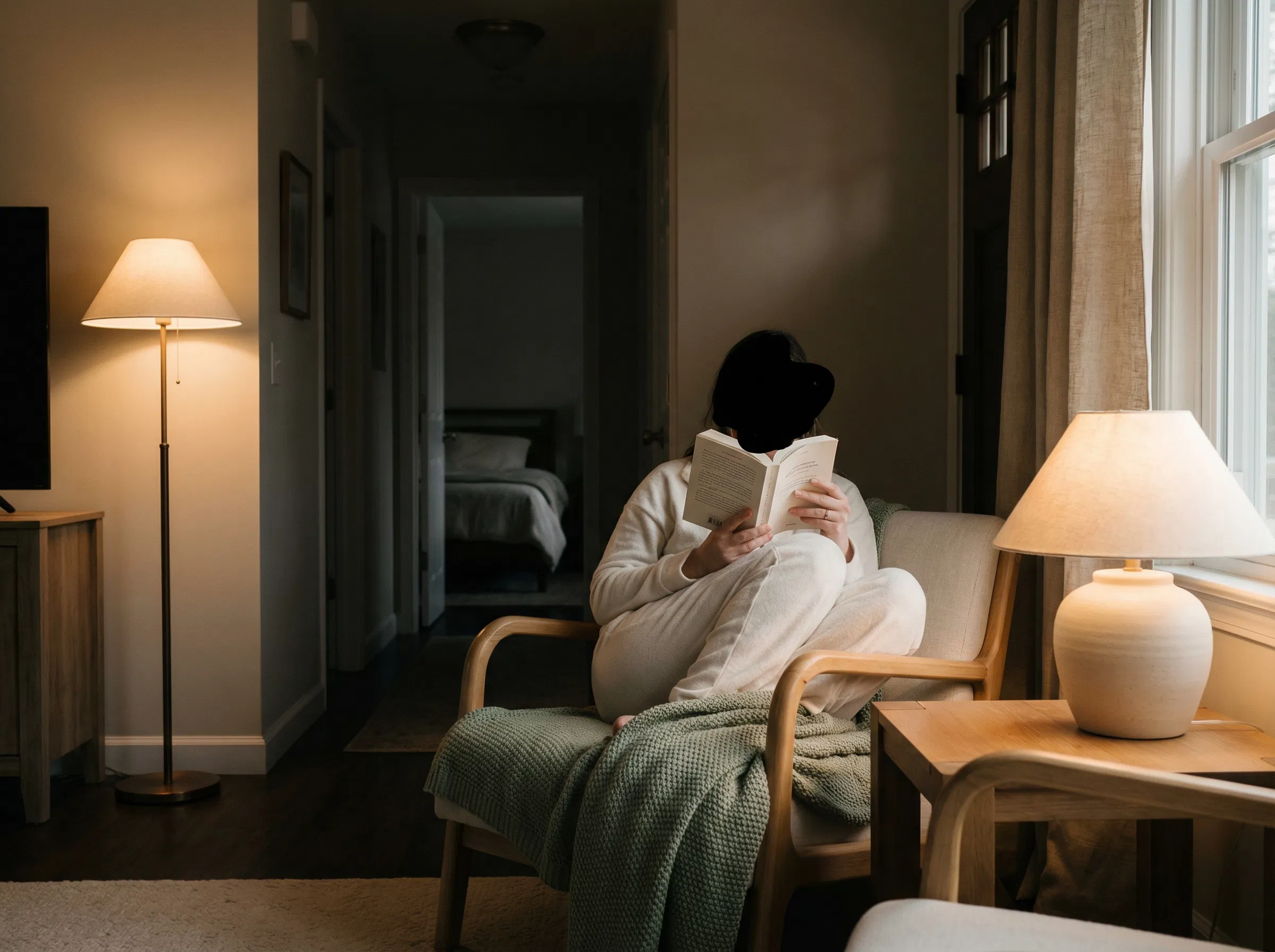 Persona leyendo en un sillĂłn acogedor por la noche despuĂ©s de salir del dormitorio