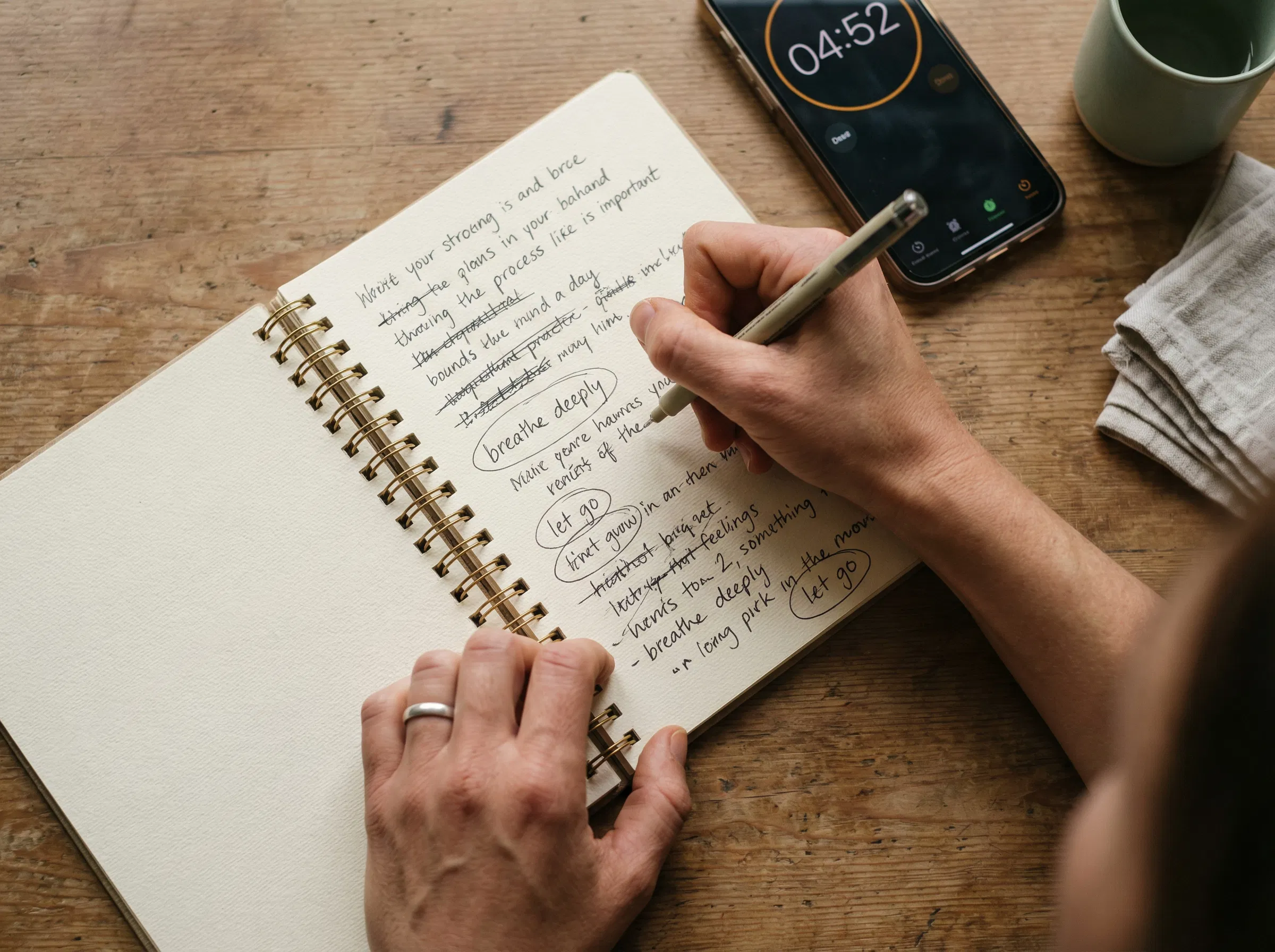 Mains écrivant rapidement dans un carnet avec texte brouillon et mots barrés, minuteur de smartphone visible, capturant l'exercice d'inventaire des pensées en action